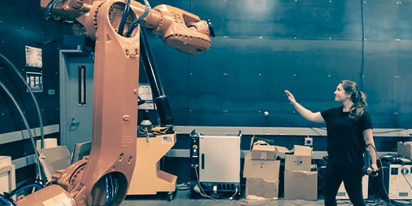 A woman in a robotics lab working in motion with a large orange robot