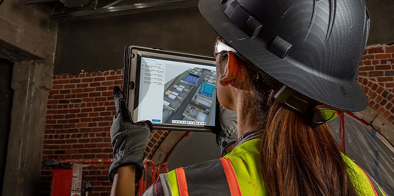 Facilities engineer comparing HVAC system in factory to 3D model of system on tablet